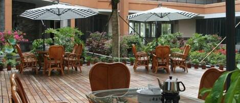 An outdoor patio with wicker furniture, umbrellas, and potted plants.