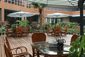 Un patio al aire libre con mobiliario de mimbre, sombrillas y plantas en macetas.