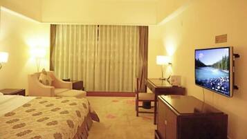 Een hotelkamer met een bed, een bureau, een stoel, een televisie en gordijnen.