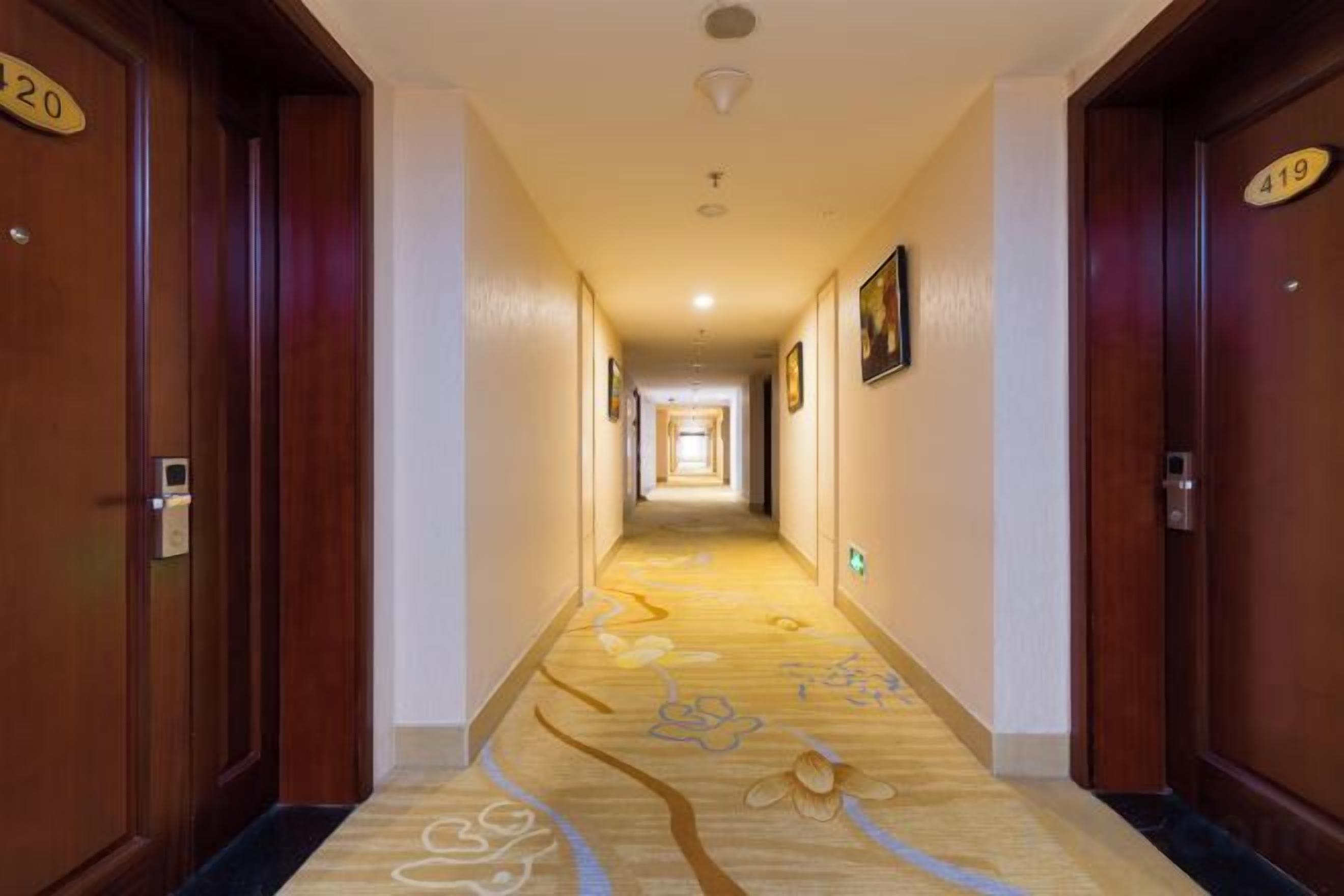 Passadís d'hotel amb portes de fusta, indicadors de número de habitació i un sòl amb moqueta.