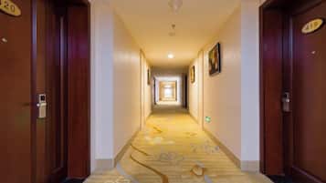 Un pasillo de hotel con puertas de madera, letreros de habitaciones numeradas y piso alfombrado.