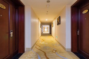 Un pasillo de hotel con puertas de madera, letreros de habitaciones numeradas y piso alfombrado.