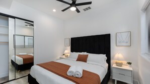 A modern bedroom with a large bed, a ceiling fan, bedside lamps, a mirror, and a framed artwork on the wall. - 2BR Midtown townhome - Walk to Golden 1 & Capitol (Sacramento)