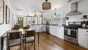 Een moderne keuken met witte kasten, een houten eettafel en een groot fornuis.