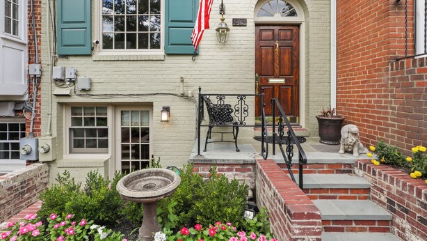 A building with a brick facade, a wooden door, and a small garden with flowers and a birdbath.