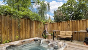 A hot tub in a backyard with a wooden fence, a chair, and a table.