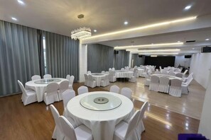 A banquet hall with round tables and chairs, a stage, and a large screen.