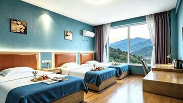 A hotel room with two beds, a wooden desk, a view of mountains, and a large window.
