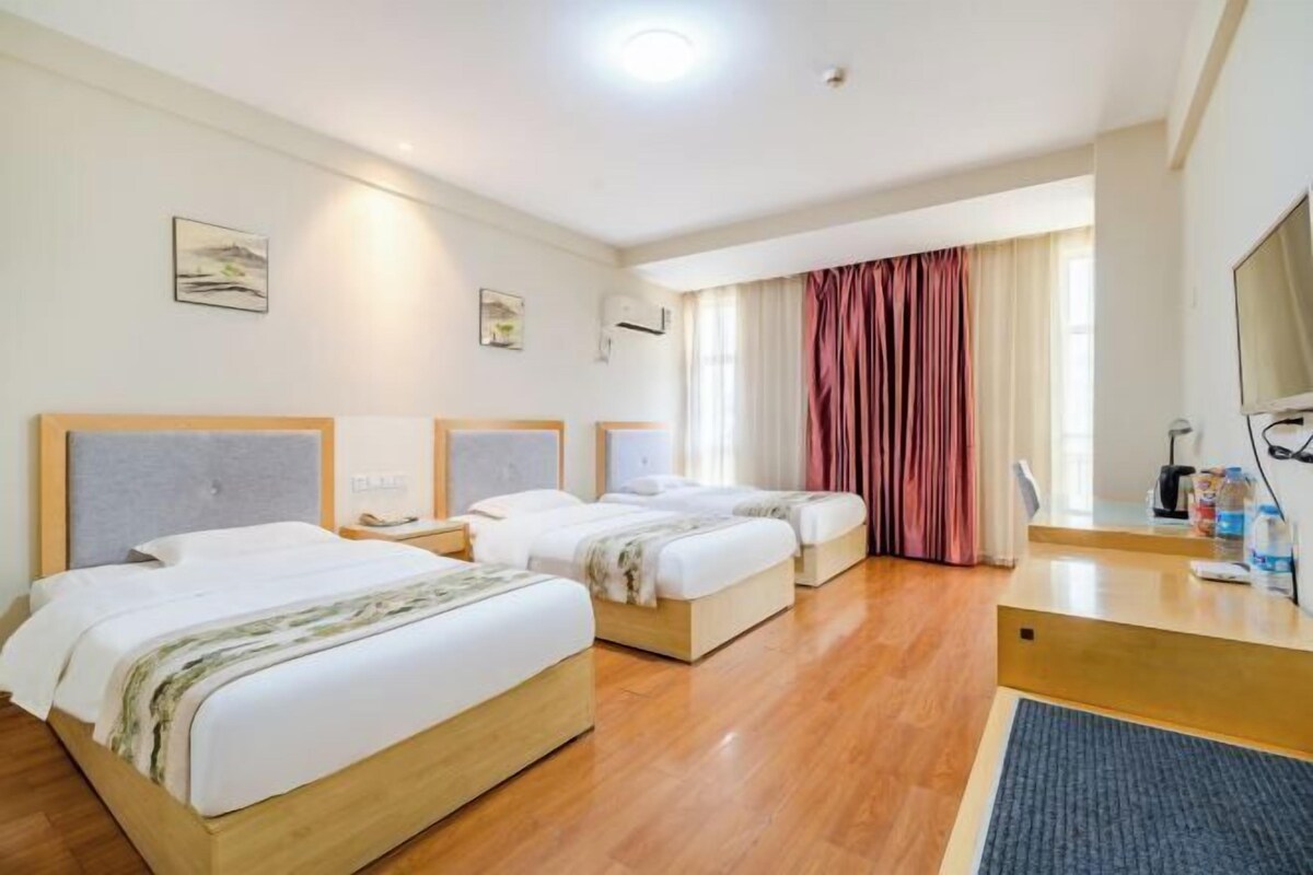 Quarto de hotel com duas camas, uma escrivaninha, uma televisão e uma janela com cortinas.
