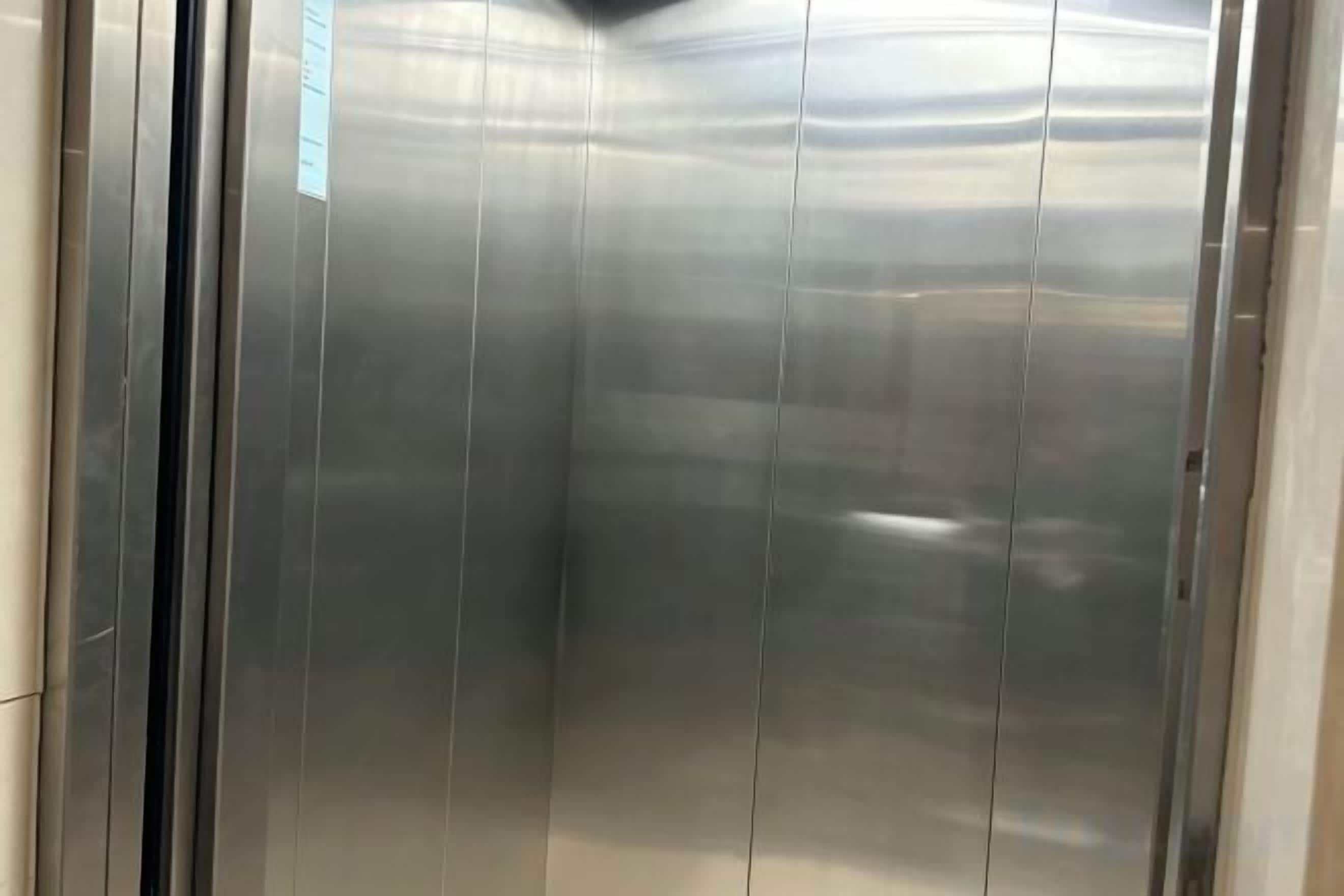 An elevator interior with metallic walls and a reflective surface.