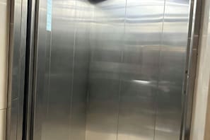 Interior de ascensor con paredes metálicas y superficie reflectante.