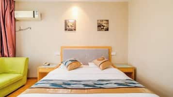 A hotel room with a bed, a green sofa, a nightstand with a phone, and two wall-mounted pictures.