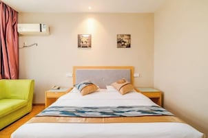 Habitación de hotel con una cama, un sofá verde, una mesita de noche con un teléfono y dos cuadros colgados en la pared.