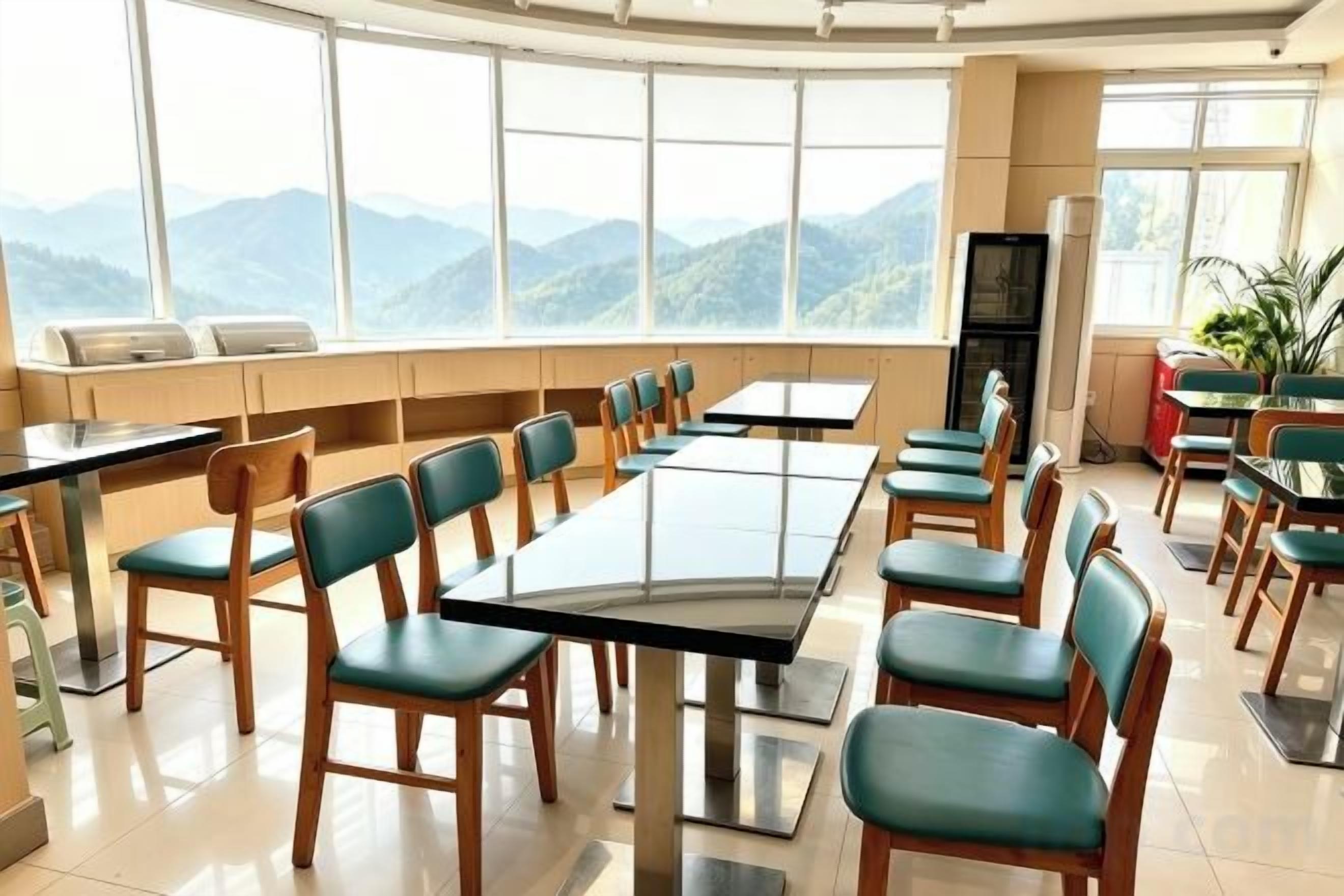 Un comedor con mesas y sillas, ventanas amplias con vistas a la montaña y un refrigerador.