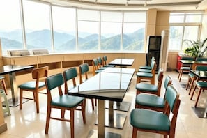 Un comedor con mesas y sillas, ventanas amplias con vistas a la montaña y un refrigerador.