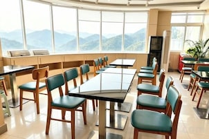 Un comedor con mesas y sillas, ventanas amplias con vistas a la montaña y un refrigerador.