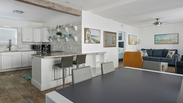 A modern kitchen with white cabinets, a marble countertop, and a dining area with a black table and chairs. - Spacious 1 Bedroom APT at the beach (Hollywood)