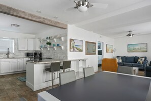 Una cocina moderna con armarios blancos, encimera de mármol y zona de comedor con mesa y sillas negras.