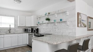 A modern kitchen with white cabinets, a granite countertop, and a bar area with two stools. - Spacious 1 Bedroom APT at the beach (Hollywood)