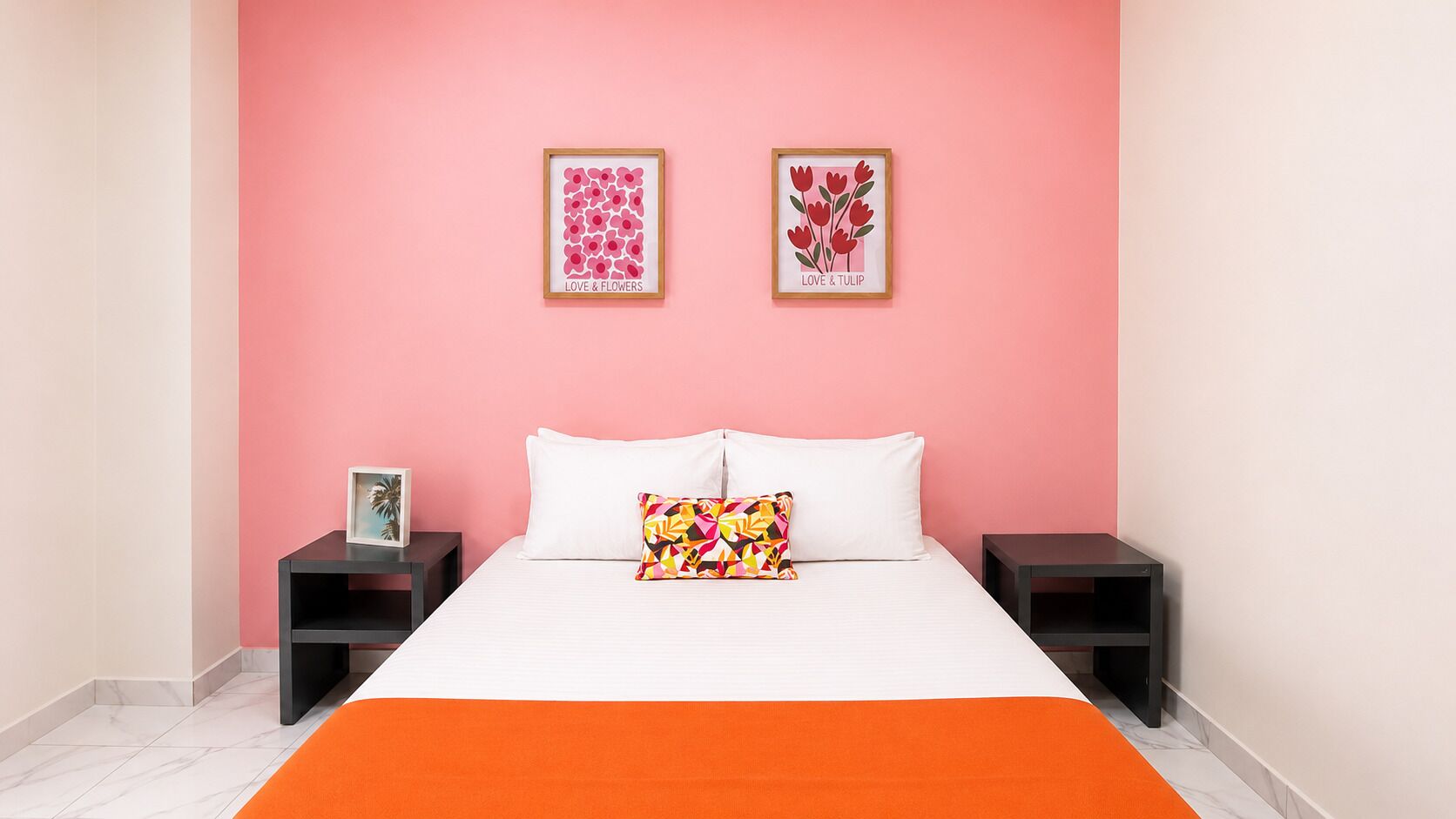 A bedroom with a bed, two nightstands, a pink wall, and two framed pictures.