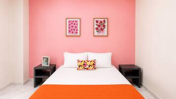 A bedroom with a bed, two nightstands, a pink wall, and two framed pictures.