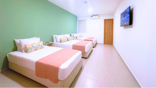 A hotel room with two beds, a green wall, a flat-screen TV, and an air conditioning unit. - Taybo Kai Hotel by St Hoteles (Santa Marta)
