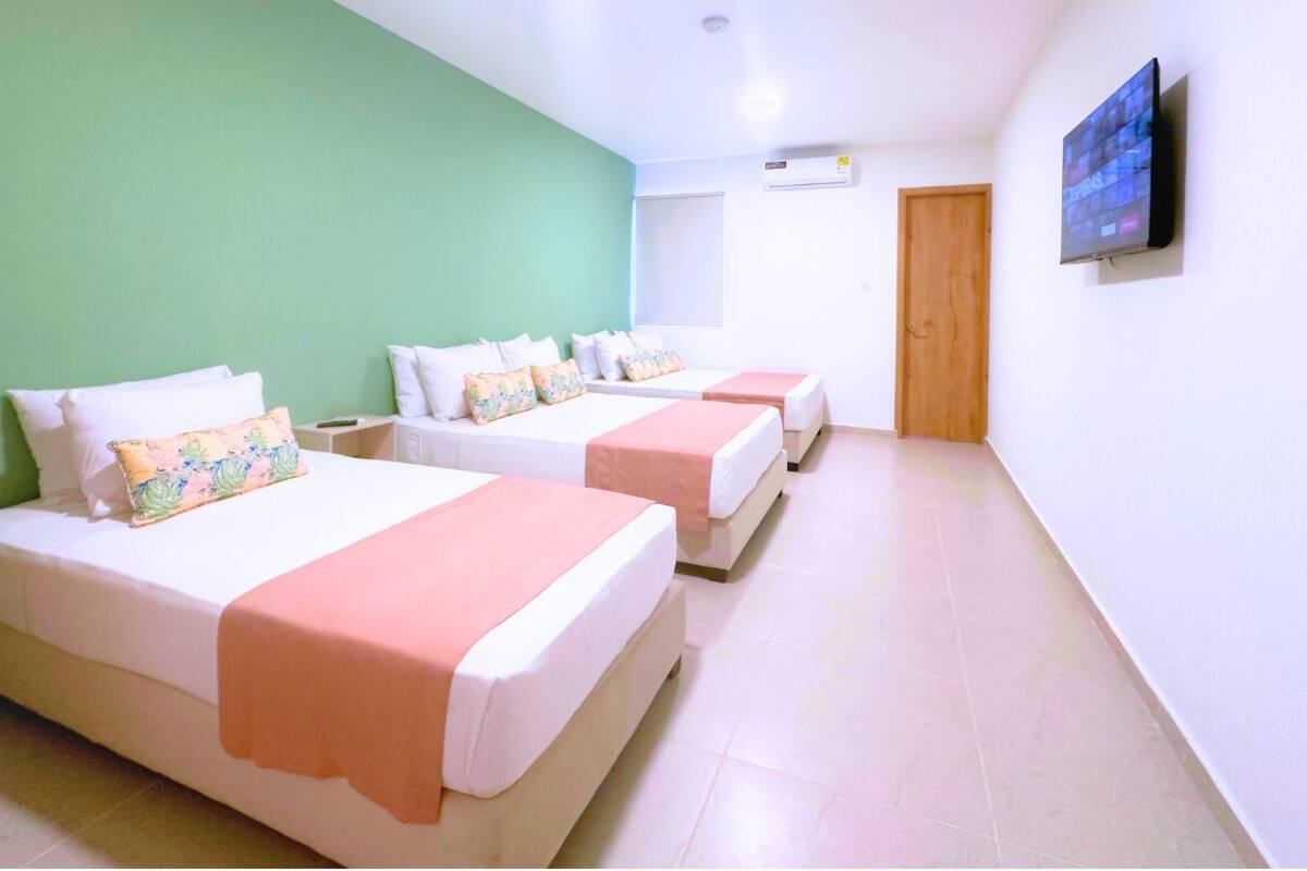 Une chambre d’hôtel avec deux lits, un mur vert, un téléviseur à écran plat et un appareil de climatisation.