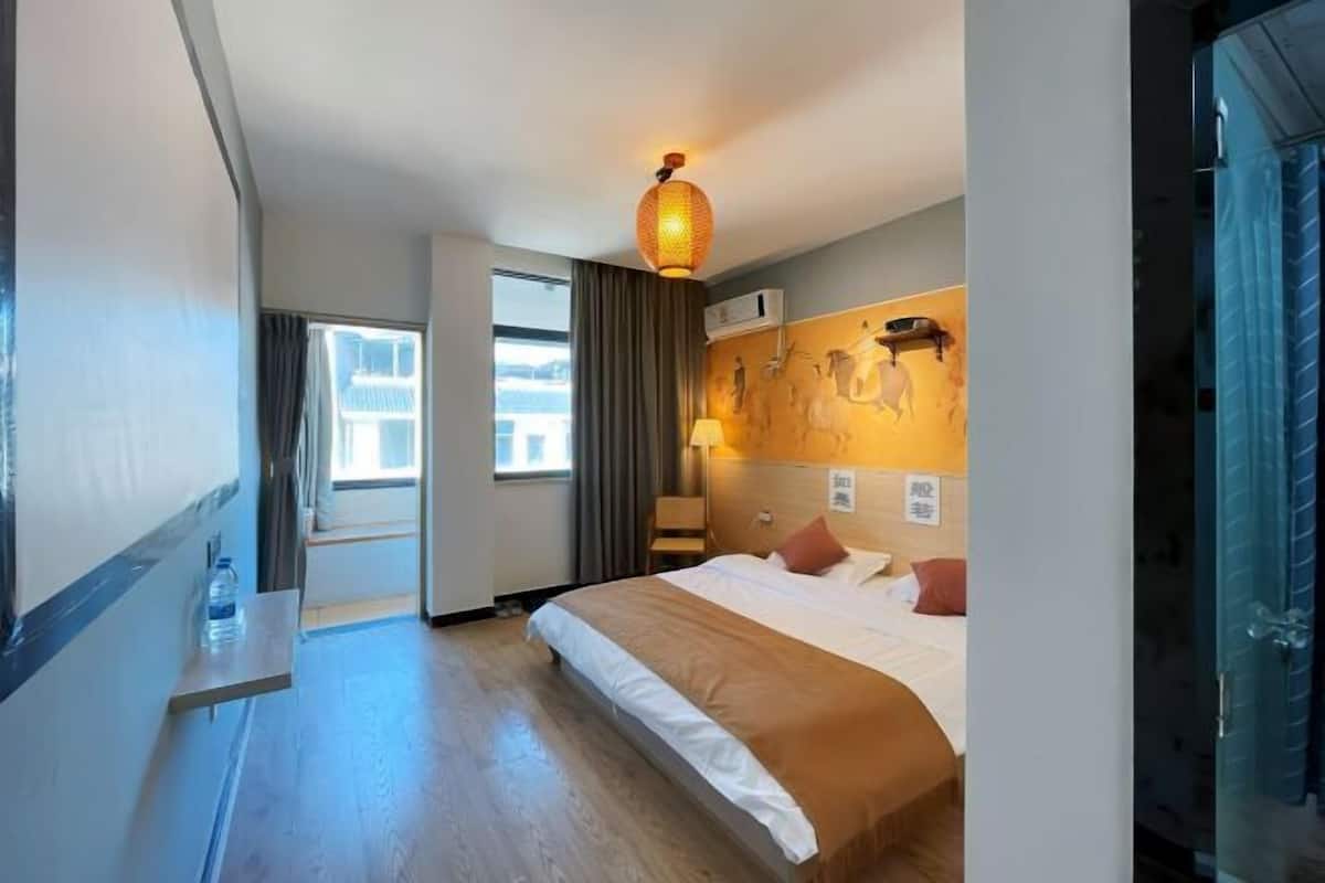 A hotel room with a bed, a nightstand, a lamp, a window, and a door.