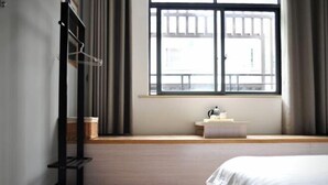 Un dormitorio con una cama, una ventana con cortinas, una mesita de noche y una estantería con una cesta.