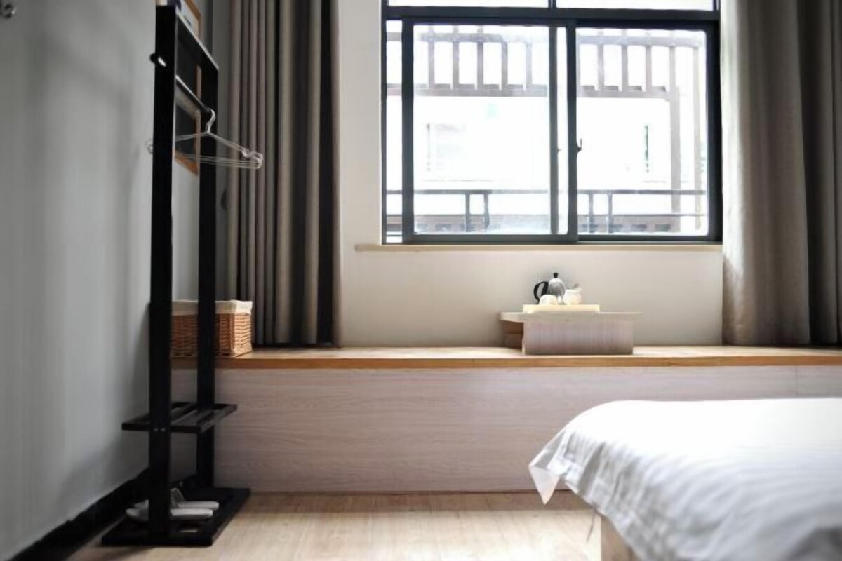 A bedroom with a bed, a window with curtains, a bedside table, and a shelf with a basket.