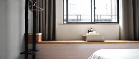 A bedroom with a bed, a window with curtains, a bedside table, and a shelf with a basket.