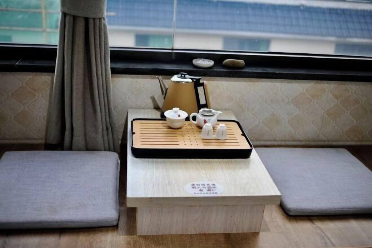 A small wooden table with a tea set and a kettle, placed on a windowsill with a view of buildings outside.