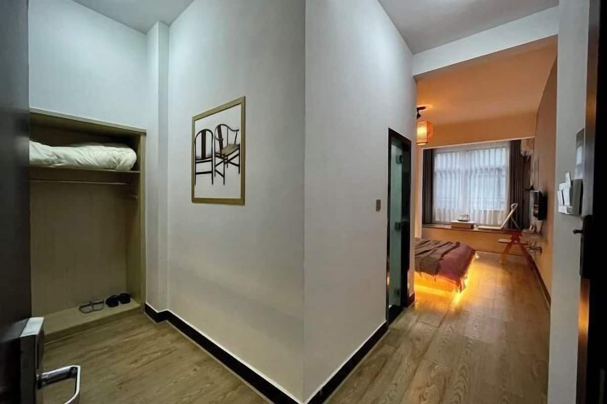 A room with a bed, a coat rack, a framed picture on the wall, and a window with curtains.
