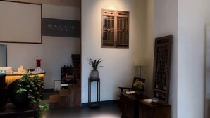 Una zona de recepción con un mostrador de madera, una planta en maceta y una puerta de madera tradicional.