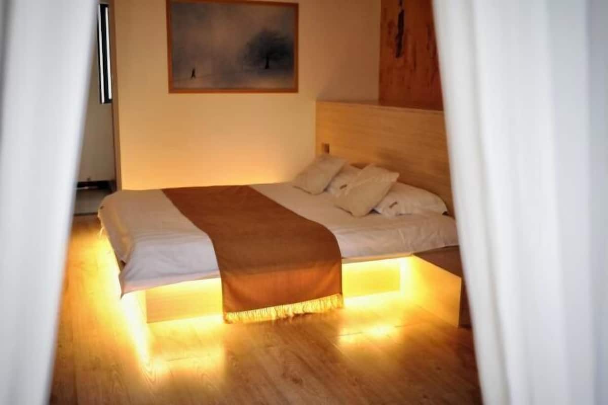 A bed with a wooden headboard, white bedding, and a brown throw blanket.