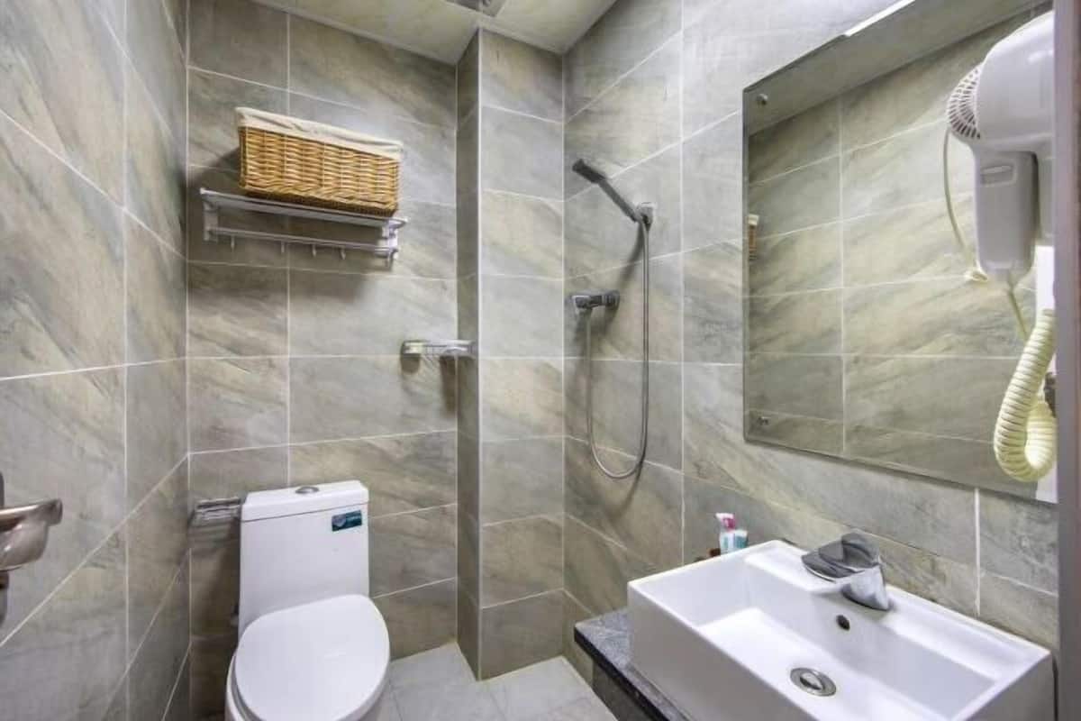 A bathroom with a toilet, a shower with a handheld showerhead, a sink, and a hairdryer mounted on the wall.
