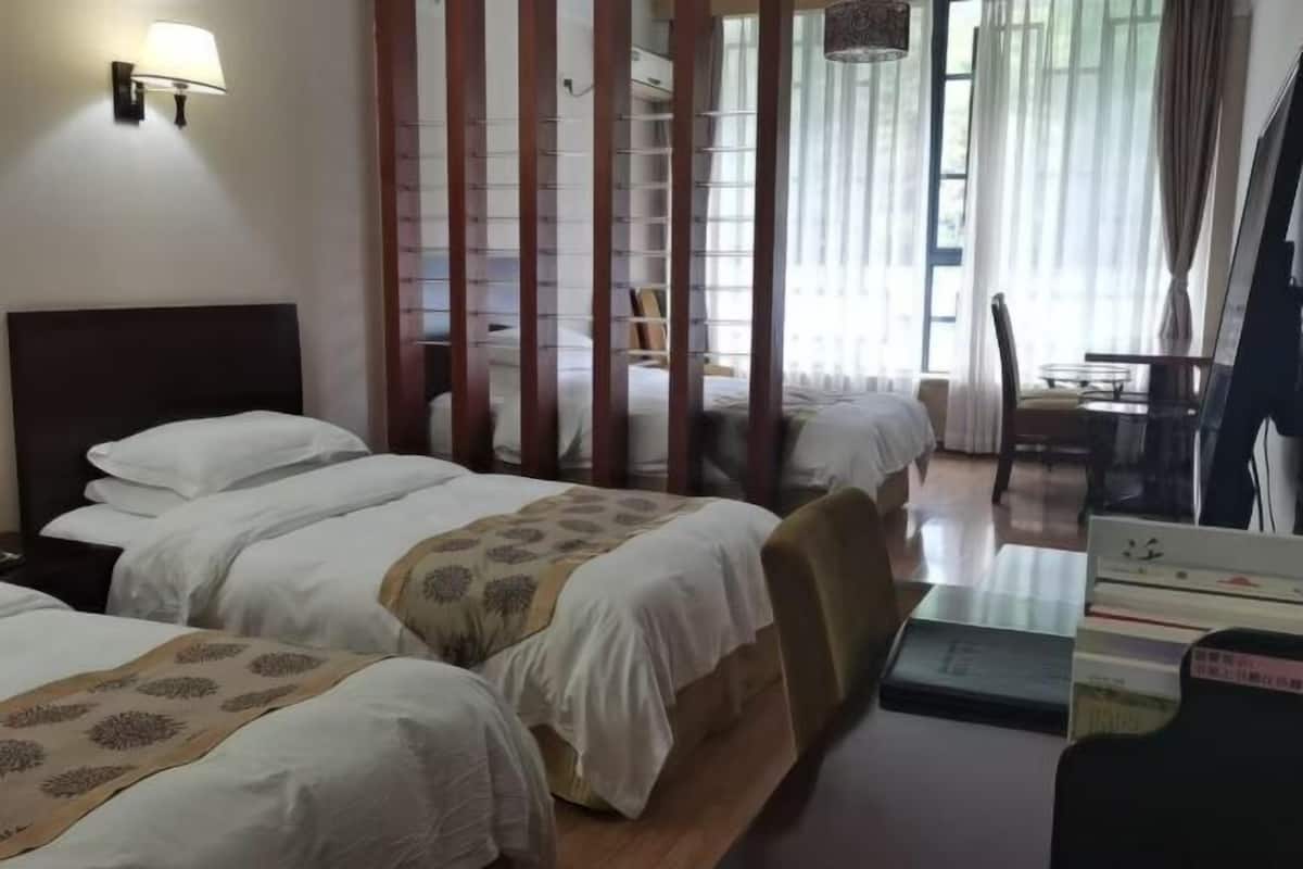 Una habitación de hotel con dos camas, un escritorio, una silla, una lámpara y un ventanal con cortinas.