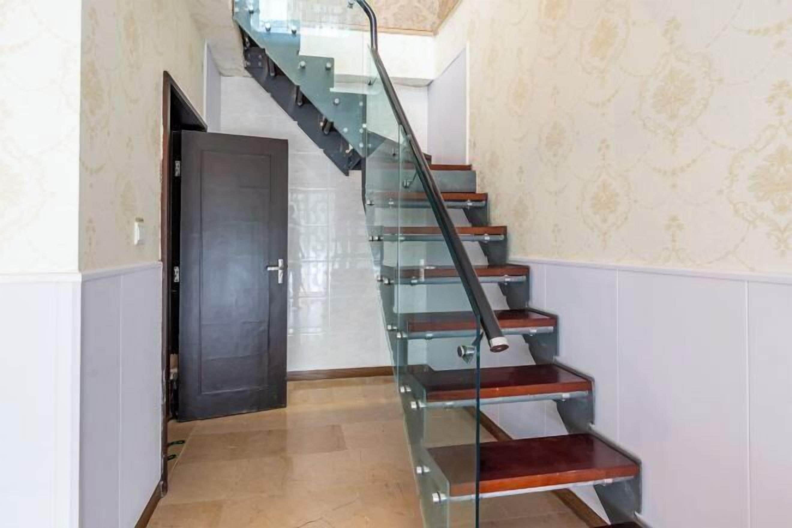 A modern staircase with glass railings and wooden steps, leading to a door at the top.