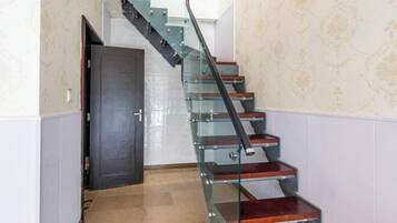 A modern staircase with glass railings and wooden steps, leading to a door at the top.