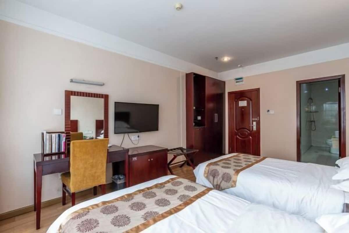Habitación de hotel con dos camas, un escritorio con silla, televisión y armario.