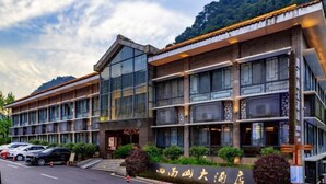 A modern hotel with a glass facade, multiple floors, and a parking lot with several cars. - Simianshan Hotel (Chongqing)