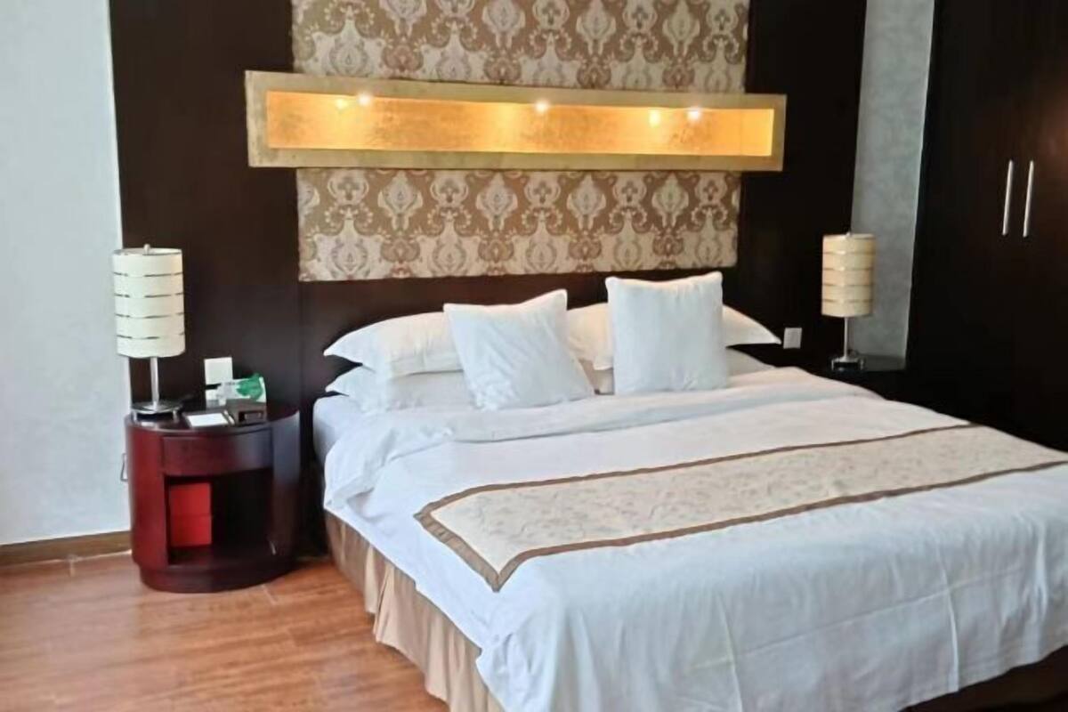 Una habitación de hotel con una cama grande, una mesita de noche, una lámpara de pared y un papel tapiz estampado.