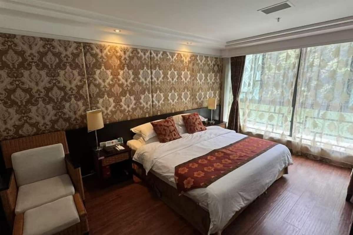 Una habitación de hotel con una cama grande, una silla, una mesita de noche y una ventana con cortinas.