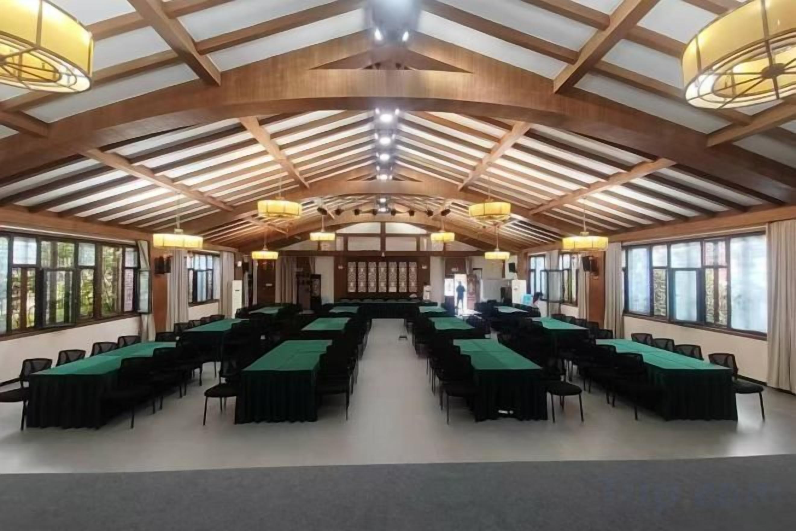 Uma sala de conferências com várias mesas e cadeiras, grandes janelas e um alto teto de madeira.