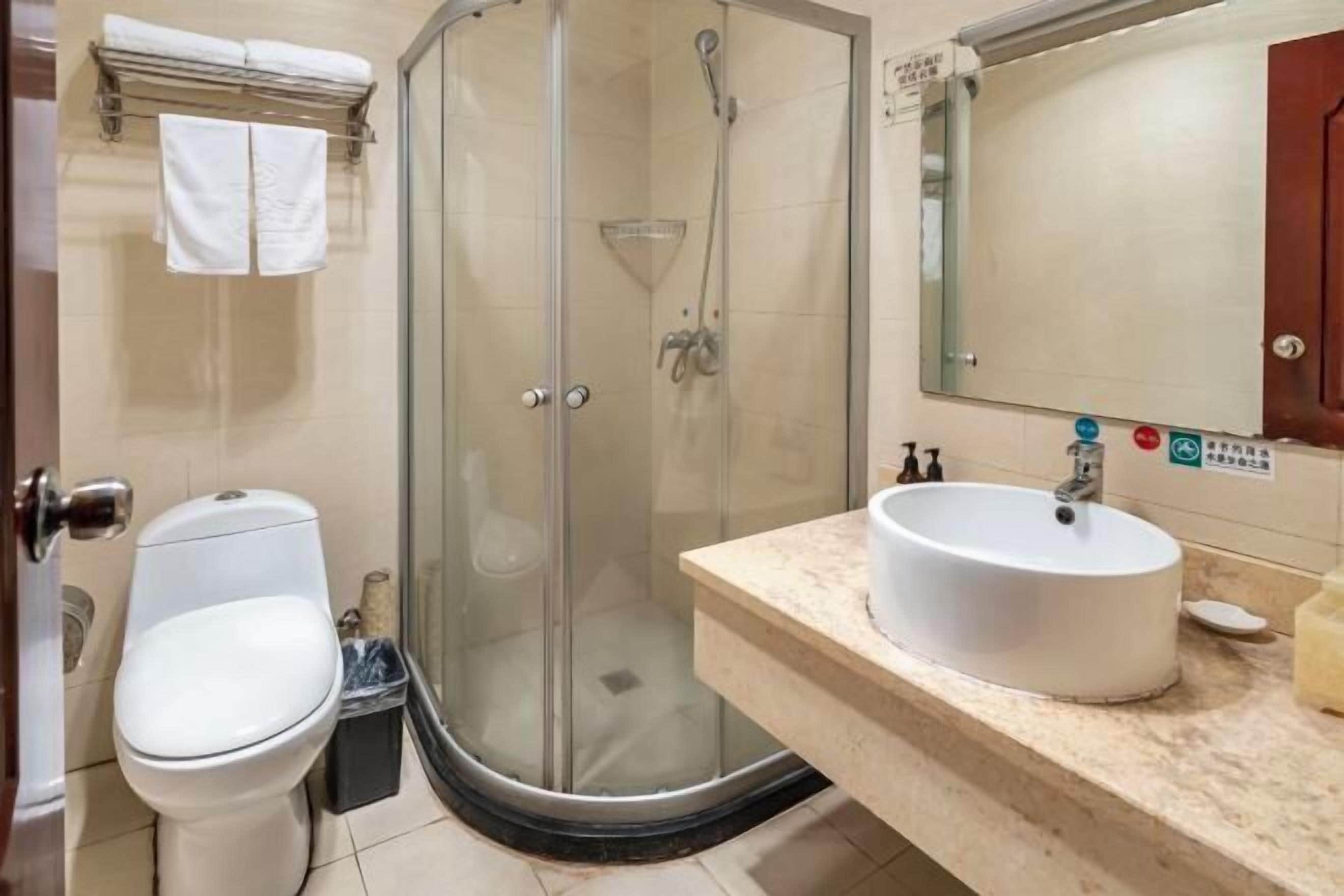 A bathroom with a glass-enclosed shower, a toilet, and a sink with a mirror above it.