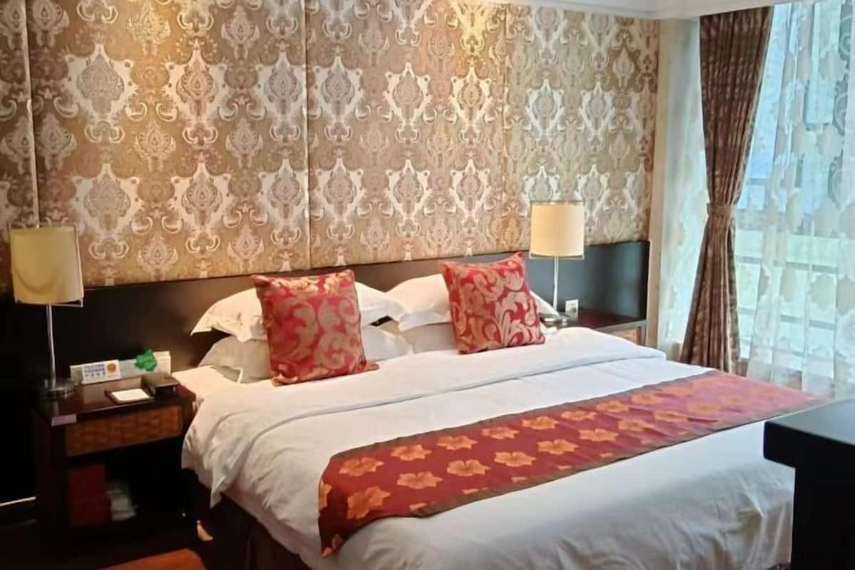 Habitación de hotel con una cama grande, dos lámparas de noche, una mesita de noche y una ventana con cortinas.