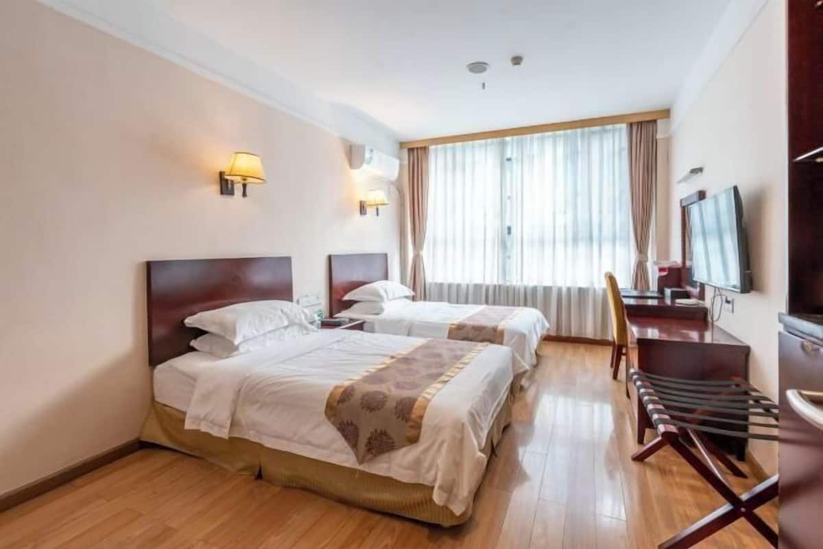 Habitación de hotel con dos camas, un escritorio con silla, televisión y un ventanal con cortinas.
