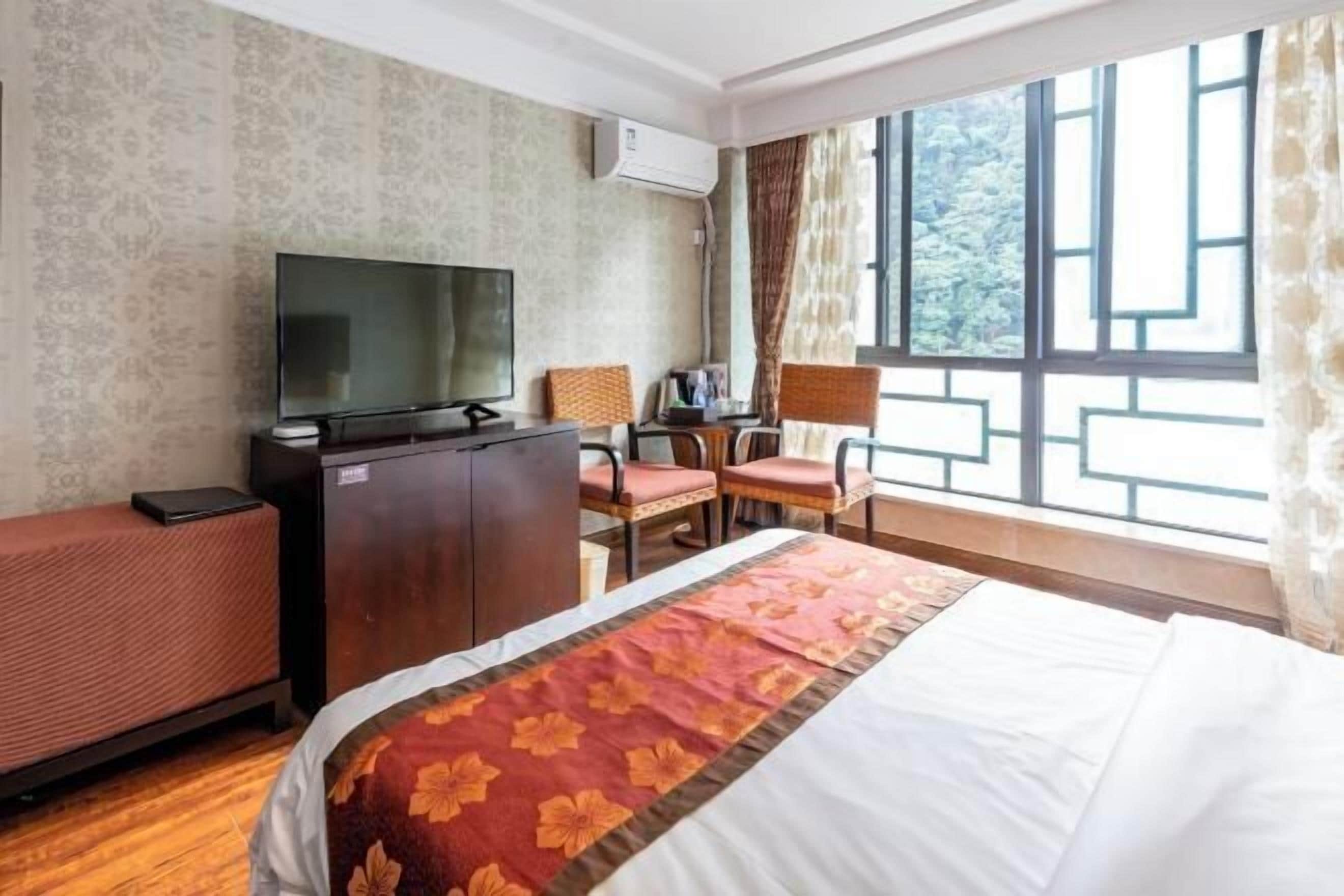A hotel room with a bed, a desk with a chair, a television, and a window with curtains.
