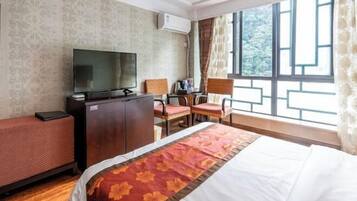 A hotel room with a bed, a desk with a chair, a television, and a window with curtains.