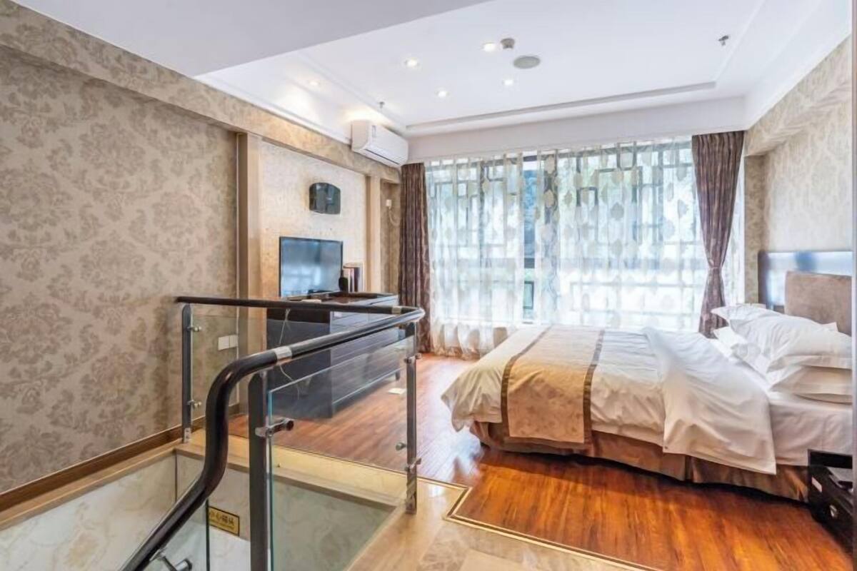 Una habitación de hotel con cama, televisión, ventana con cortinas y una escalera.